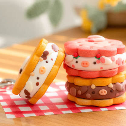 Three cute, cow-themed sandwich cookies with a keychain ring, displayed on a red and white checkered napkin on a wooden table with a soft-focus background.